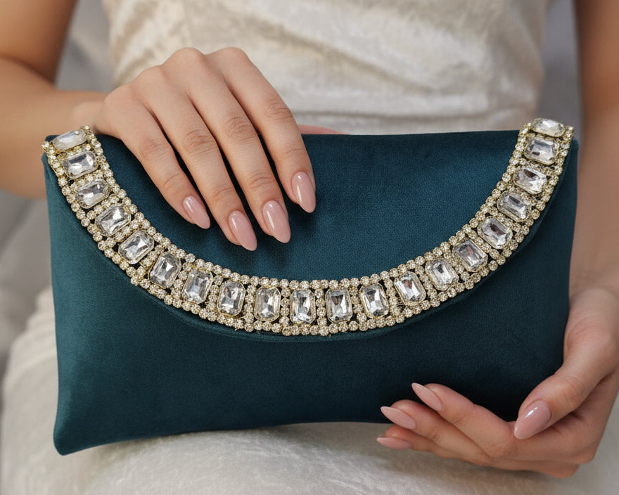 Teal clutch with crystal embellishments held by a person against a neutral background